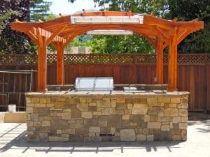 Outdoor kitchen with stone facade and wooden pergola