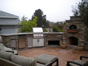 Large outdoor kitchen with a connected stone fireplace and pizza oven